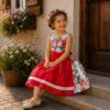 Sitzendes Mädchen im floralen Kinderdirndl Herzilein mit roter Schürze.
